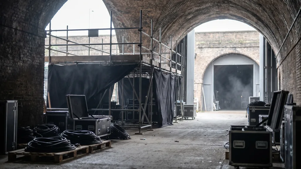 An empty London railway arch activation venue before doors, scaffold structure, coiled cables, flight cases and grey daylight