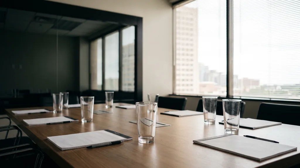 An empty Houston focus group viewing room before a session, one-way glass, water glasses on a long table, notepads, humid morning light through blinds