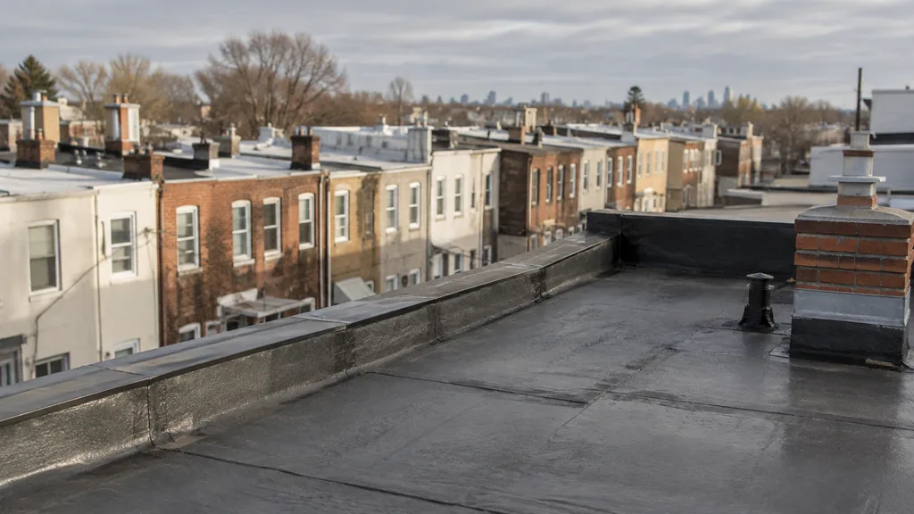 An empty roof surface: a flat modified-bitumen rowhouse roof with a neat parapet edge under soft grey Pennsylvania light