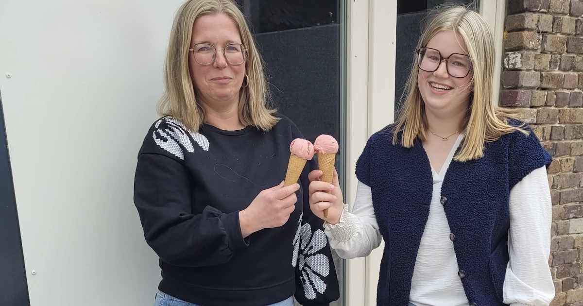 Two women smiling and holding ice cream cones with pink ice cream outdoors