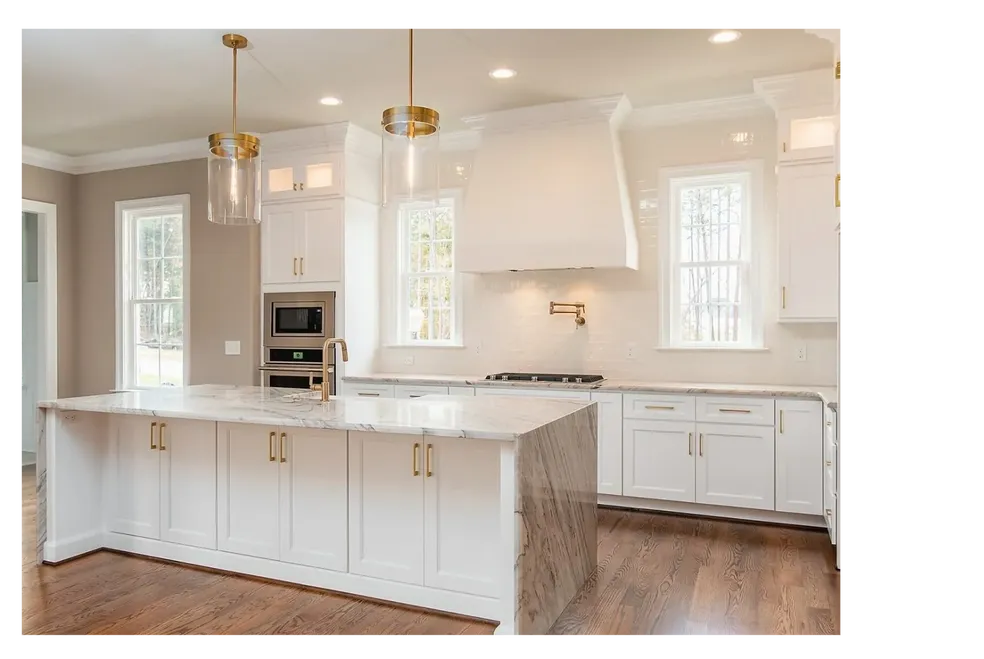 Bright kitchen with white cabinetry, marble island, brass fixtures, and hardwood floors.