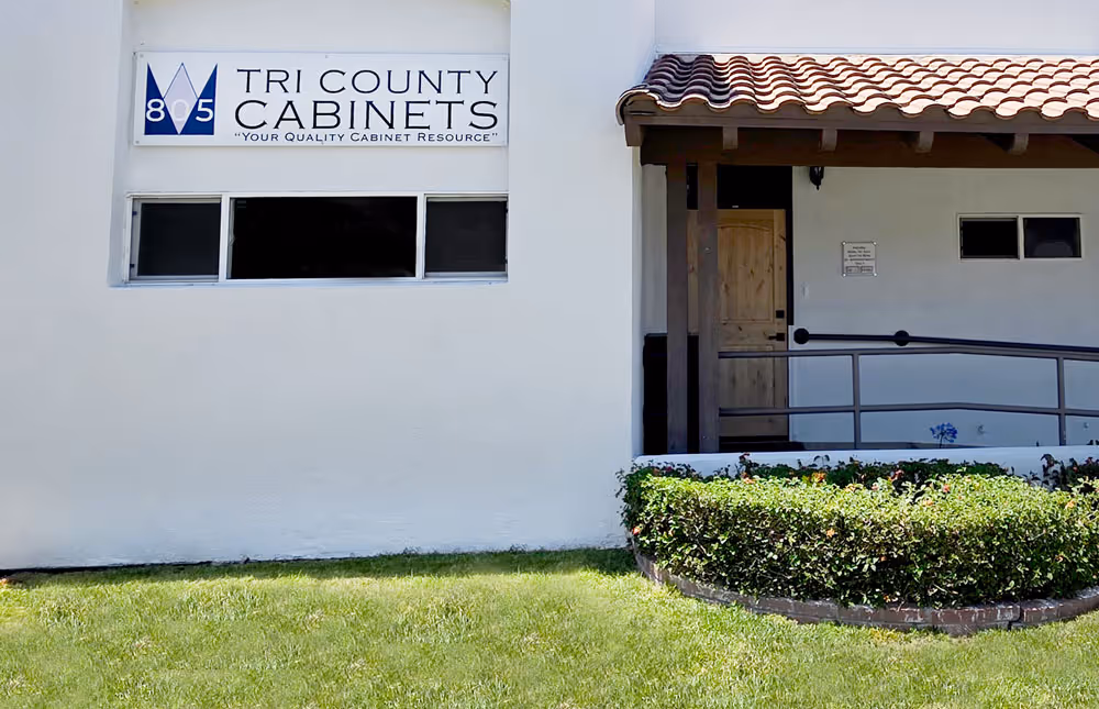Tri County Cabinets storefront with white walls, sign, covered entrance, and green lawn with trimmed bushes.