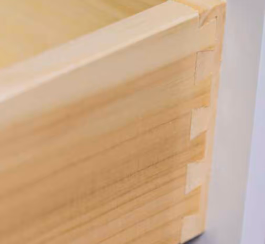 Close-up of wooden dovetail joinery connecting parts of a cabinet drawer box.