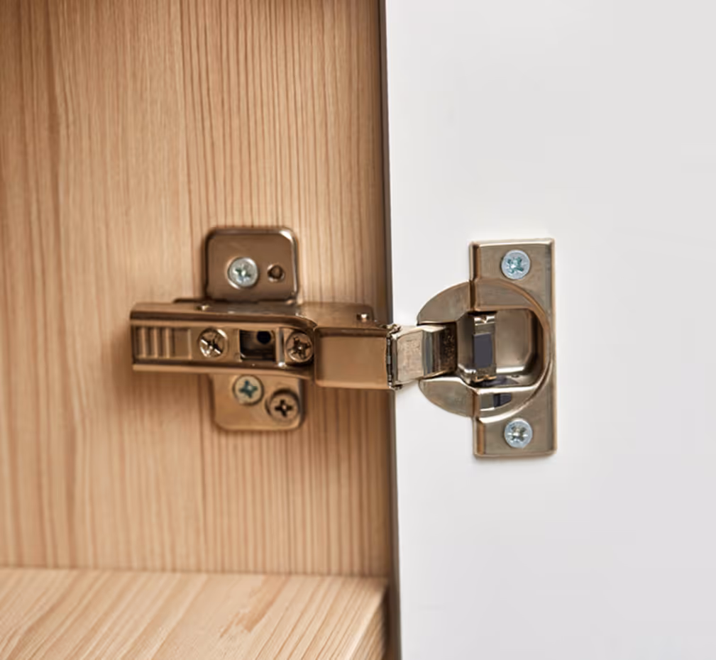 Close-up of a metal soft-close hinge connecting a wooden cabinet and a white door panel.