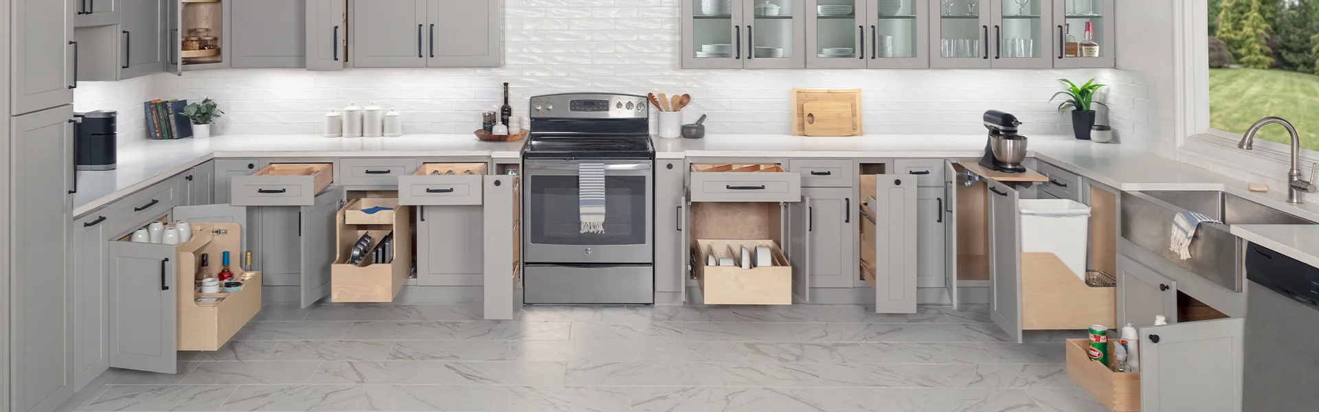 Modern kitchen with gray cabinets open to show organized pull-out drawers and shelves around a stainless oven.
