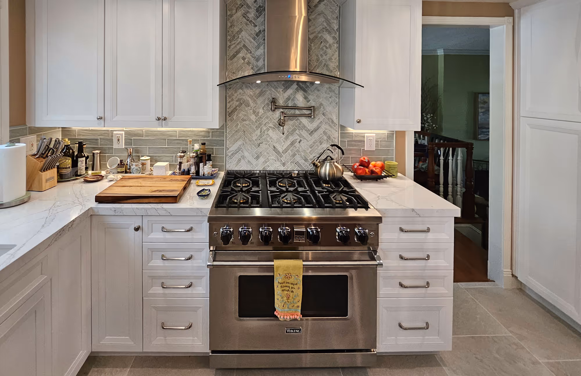 Modern kitchen with stainless steel Viking gas stove, white cabinets, marble countertops, and backsplash.