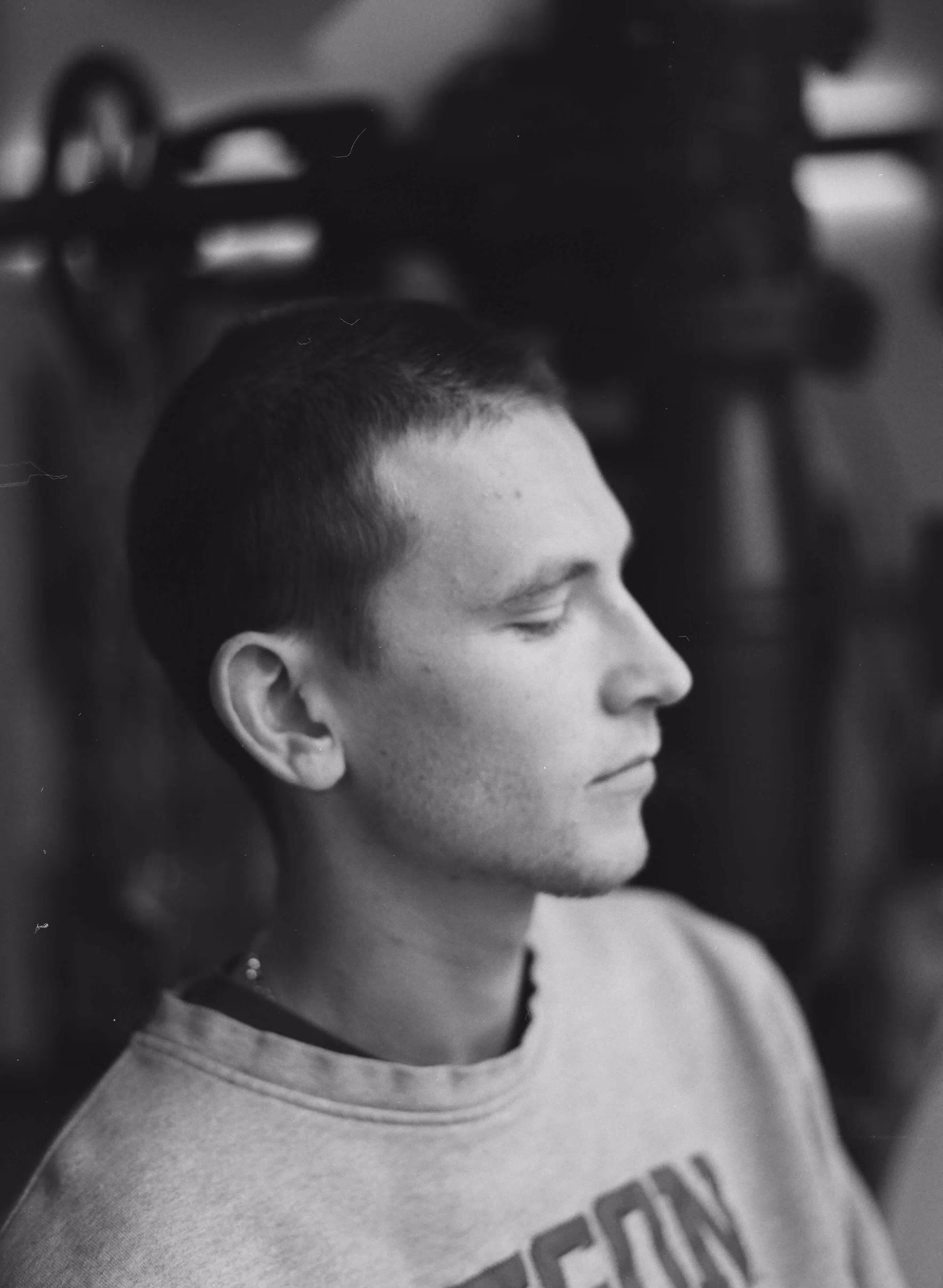Profile of a young man with short hair wearing a sweatshirt with partially visible text, eyes closed, in black and white.