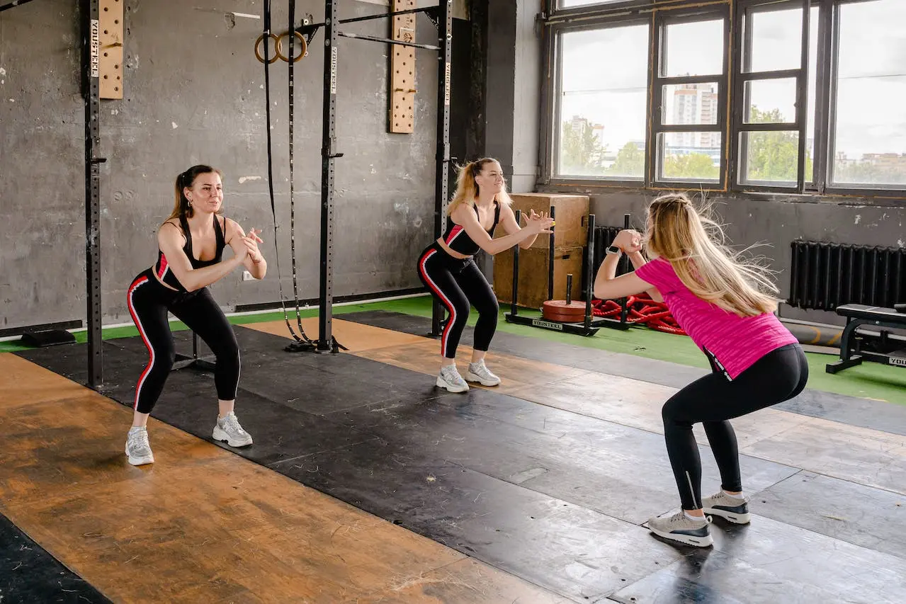 one-personal-trainer-showing-how-to-do-squats-to-her-two-students