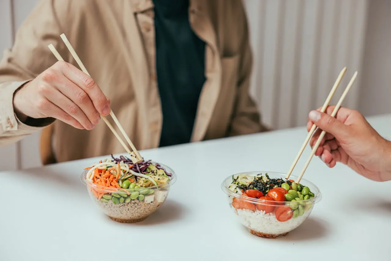 two-individuals-eating-vegetable-bowls-with-chopsticks
