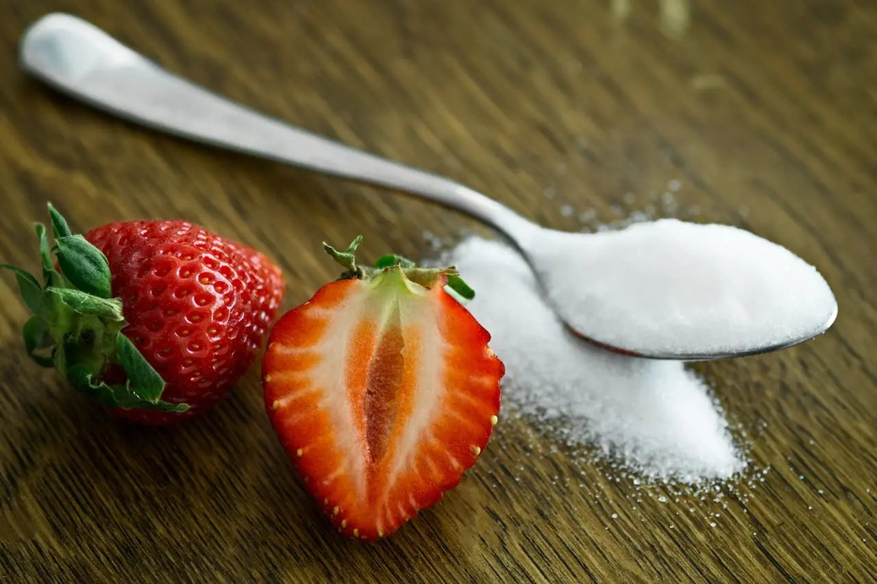 Two strawberries next to a spoon piled with sugar.