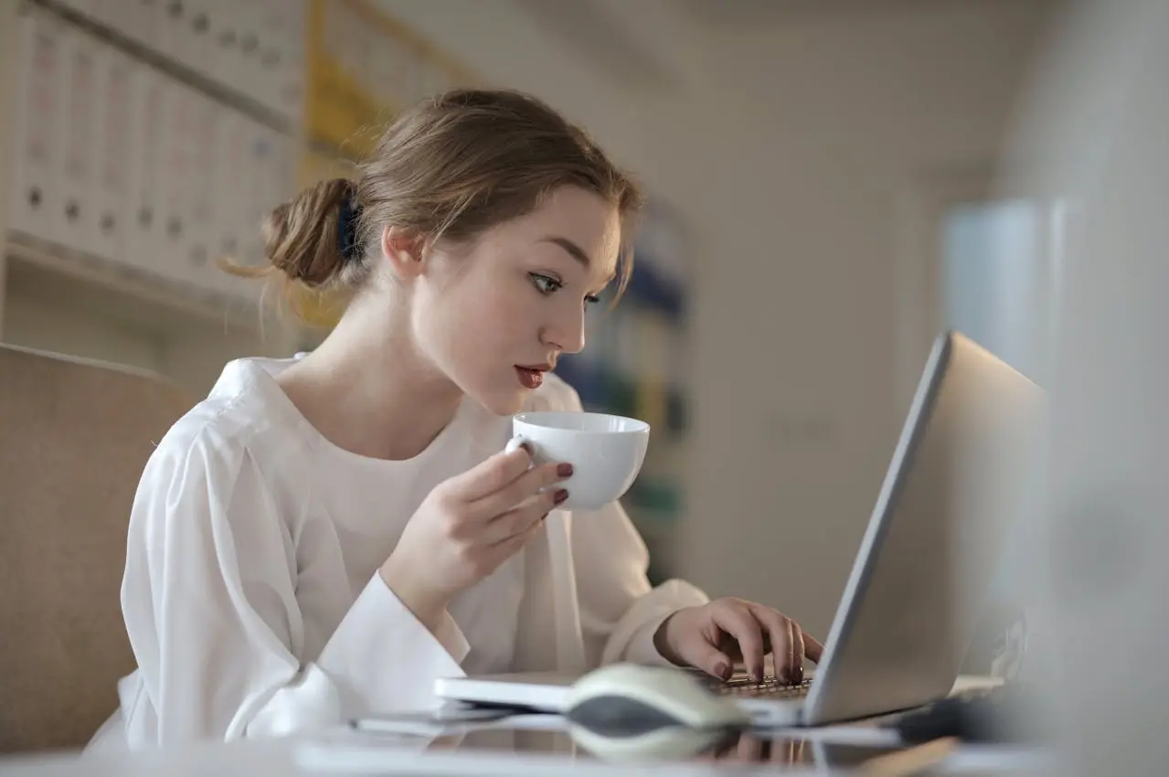 Woman multitasking: using laptop while holding a cup of coffee.