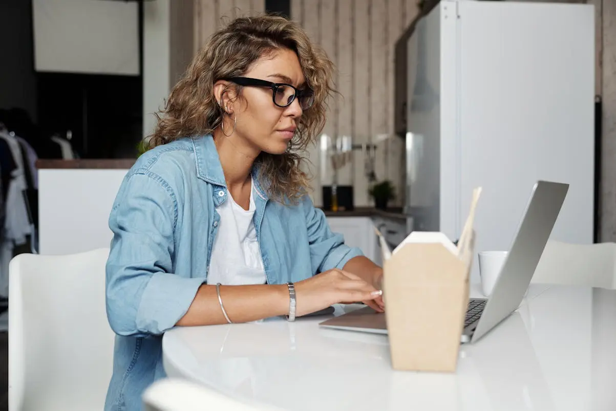 Woman using laptop with Chinese food pack beside.