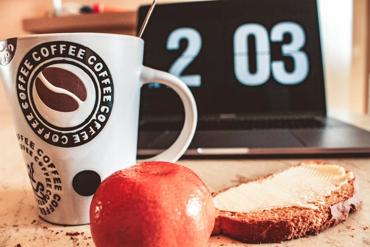 A cup of coffee, an apple, and a toast with a laptop in the background indicating 2pm