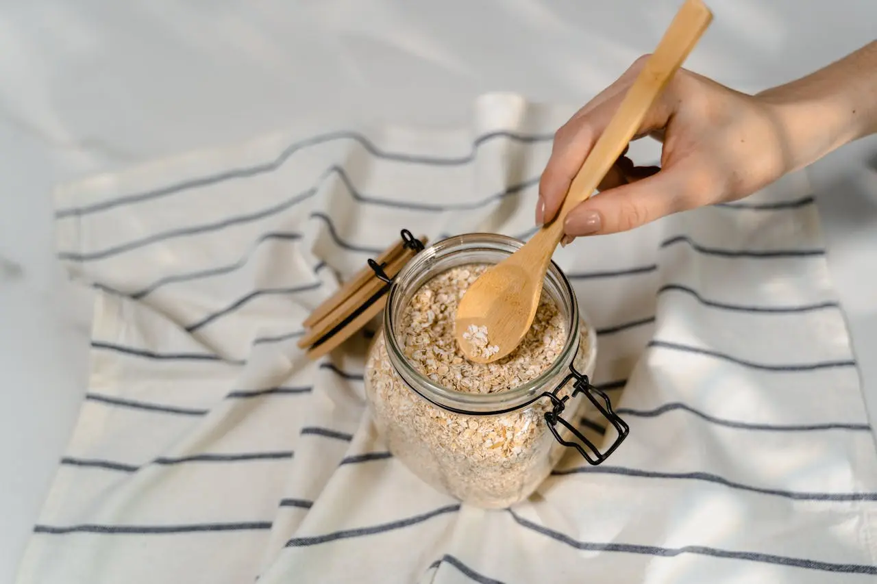 A hand using a wooden spoon to scoop oatmeal from a jar.