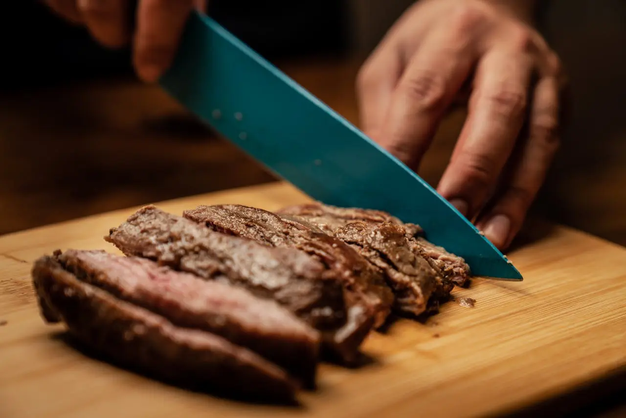 hand-chopping-a-meat-with-a-blue-knife-on-a-wooden-table