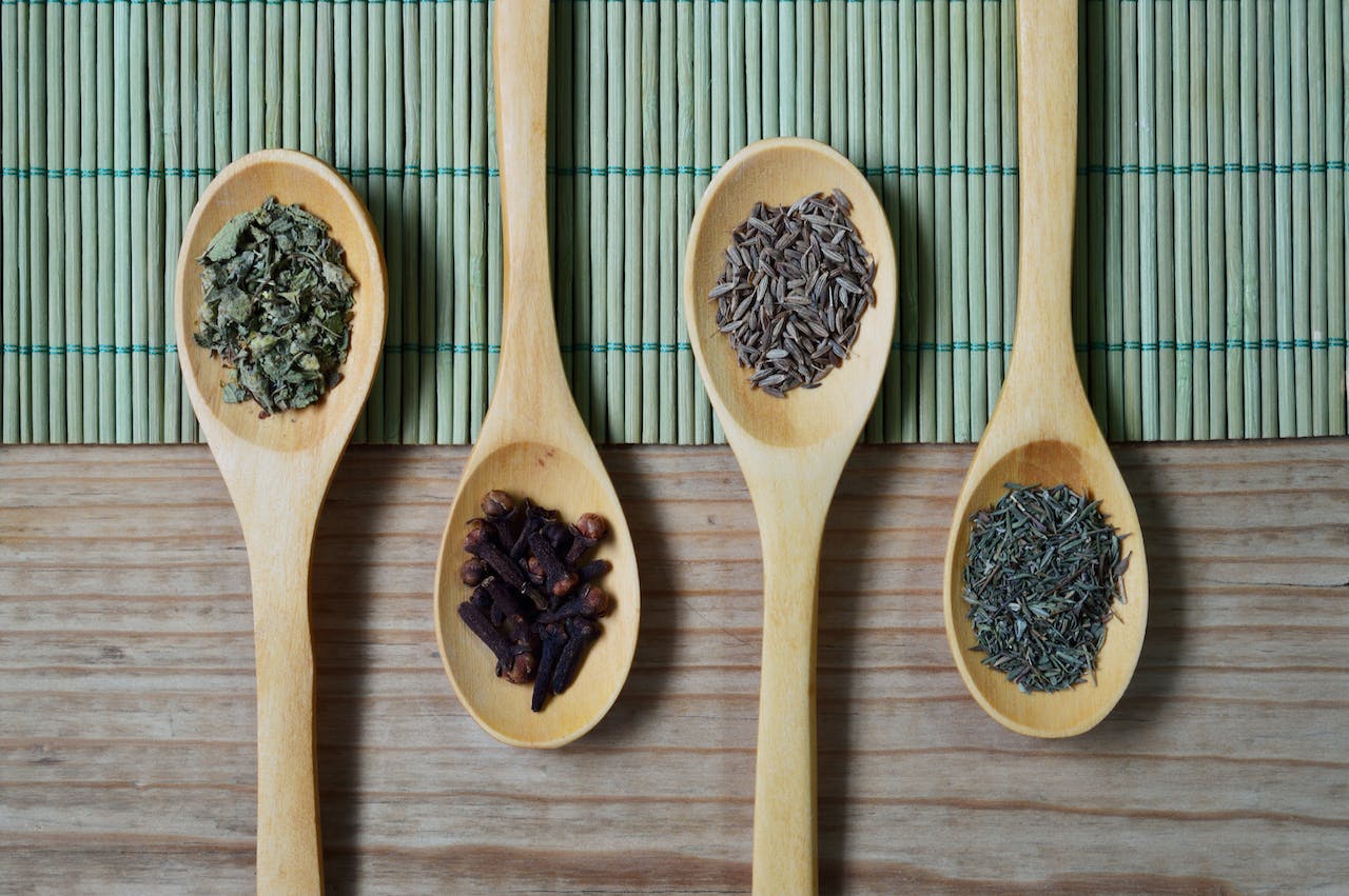 Four wooden spoons with different dried herbs and spices