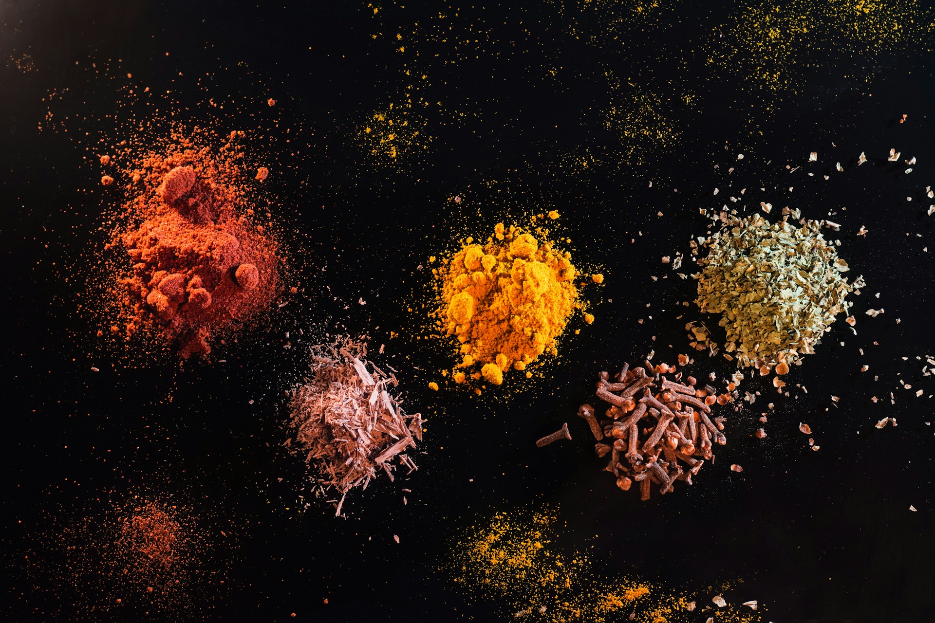Colorful spices scattered on black background, vibrant powders and seeds