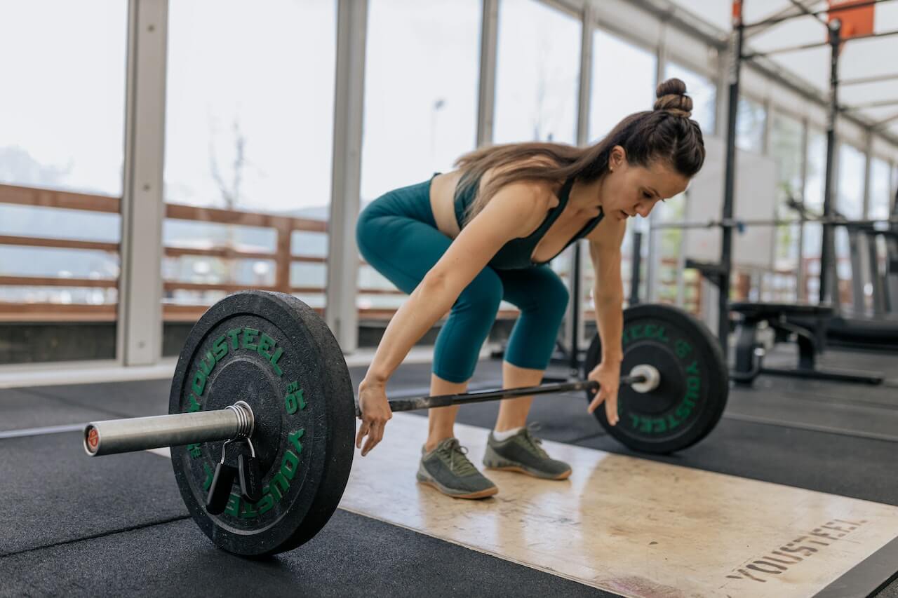 Woman in teal workout gear preparing to lift barbell in gym