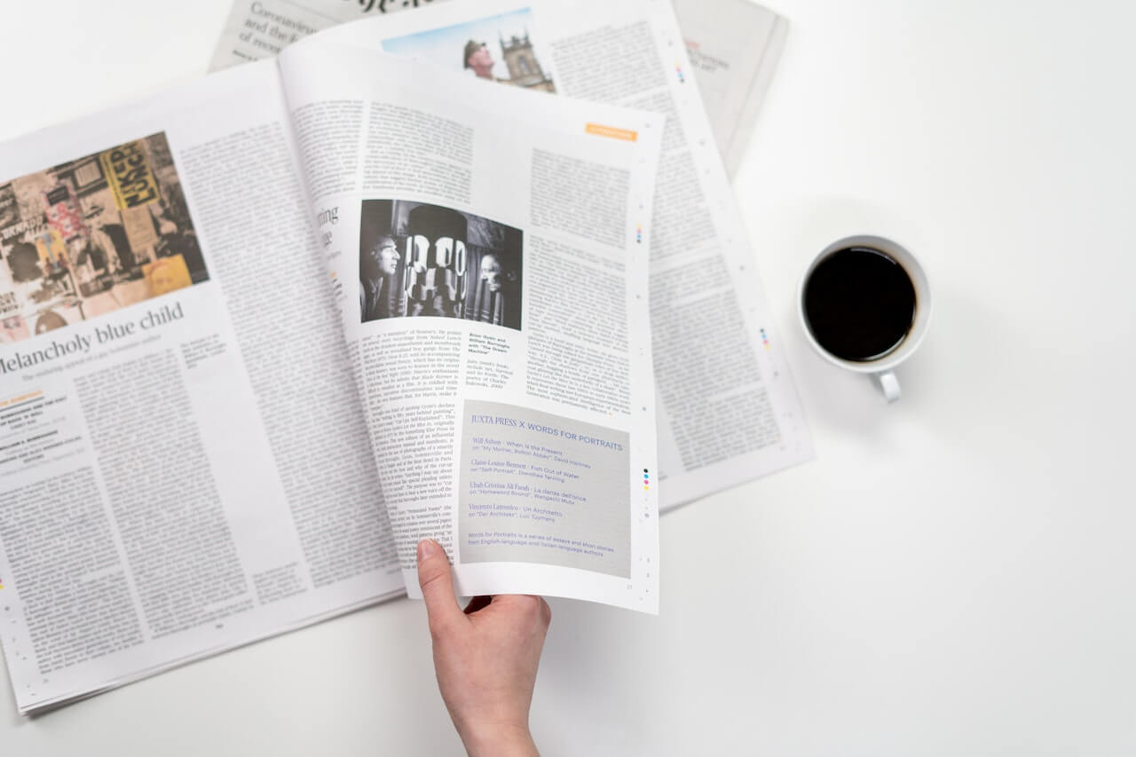 Hand holding open magazine with black and white photo, coffee nearby