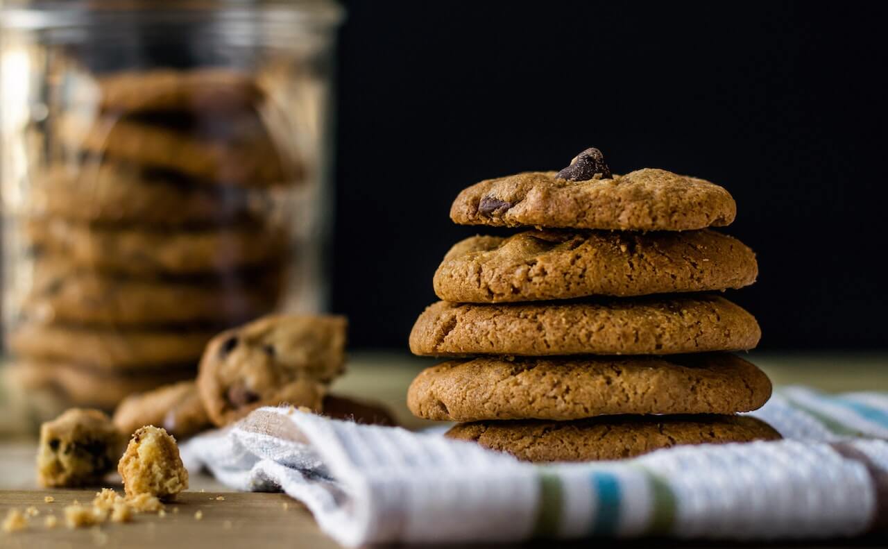 Stack of chocolate chip cookies on striped cloth with cookie jar