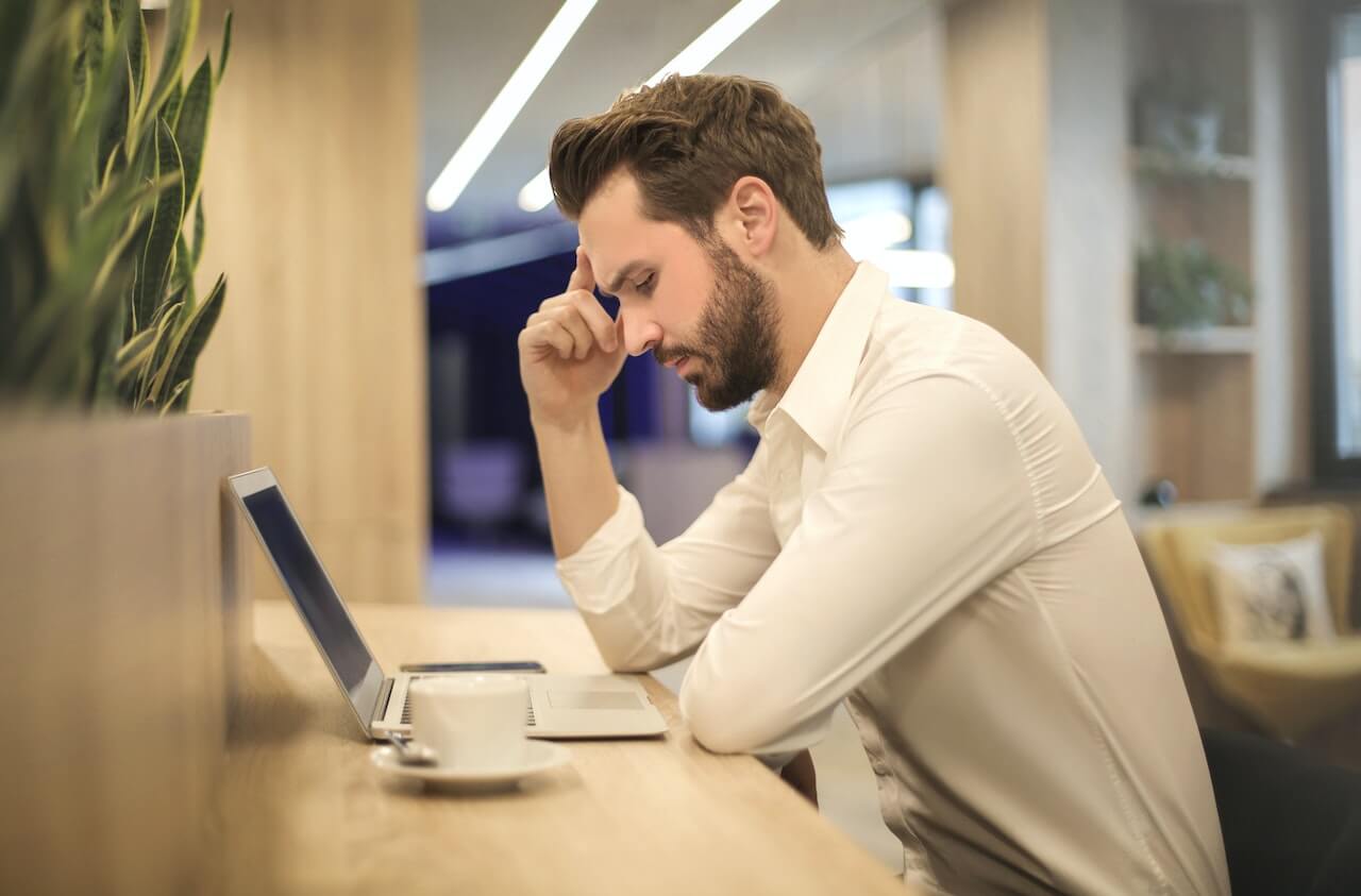 Stressed person at laptop with head in hand in modern office