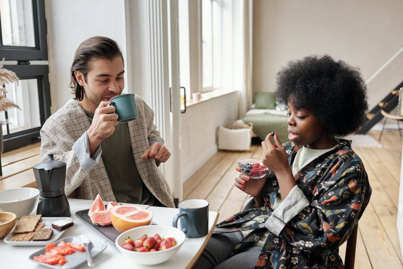 Two people enjoying breakfast with coffee, fruits, and grapefruit