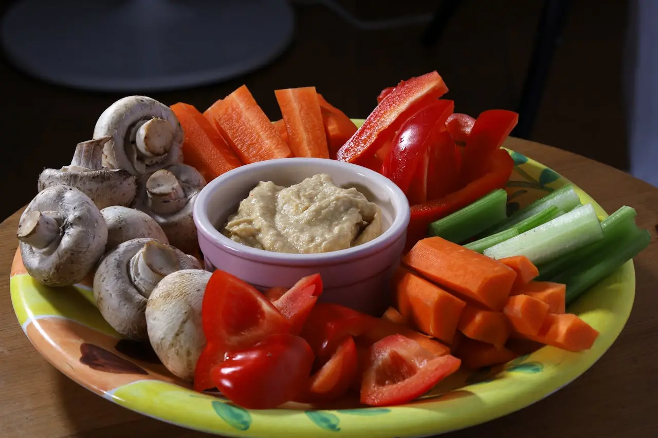 Colorful vegetable platter with hummus dip surrounded by fresh mushrooms, red peppers, and green beans