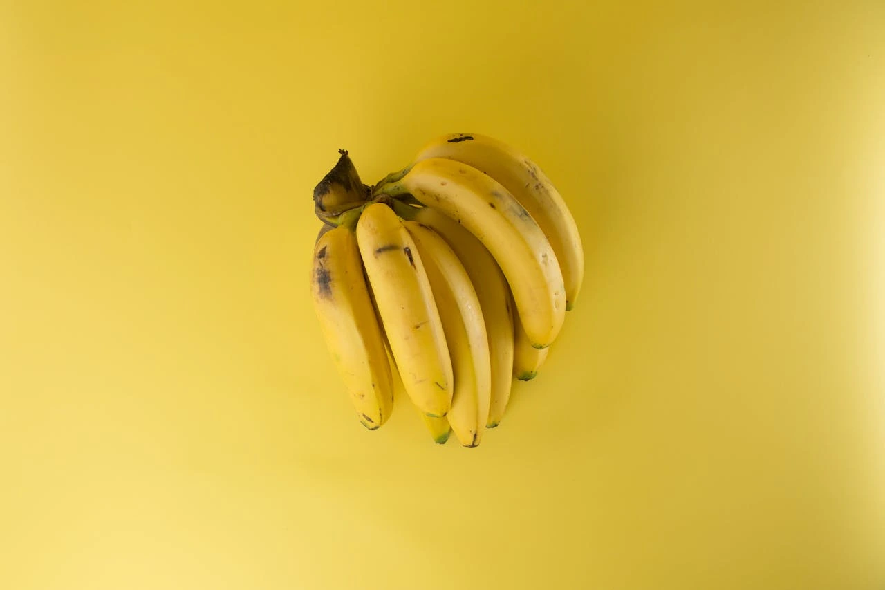A bunch of ripe yellow bananas with brown spots on a bright yellow background
