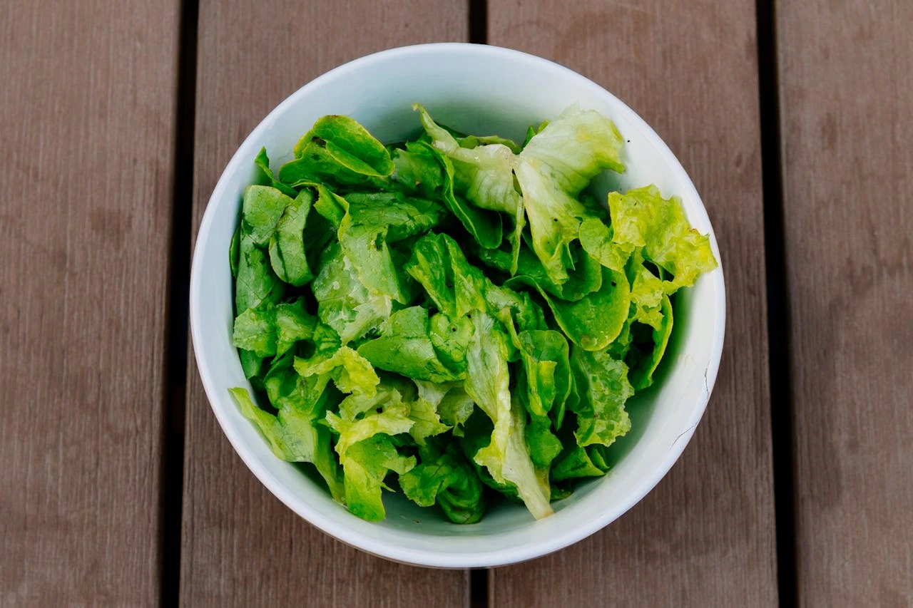Fresh mixed green lettuce in white bowl on wooden table