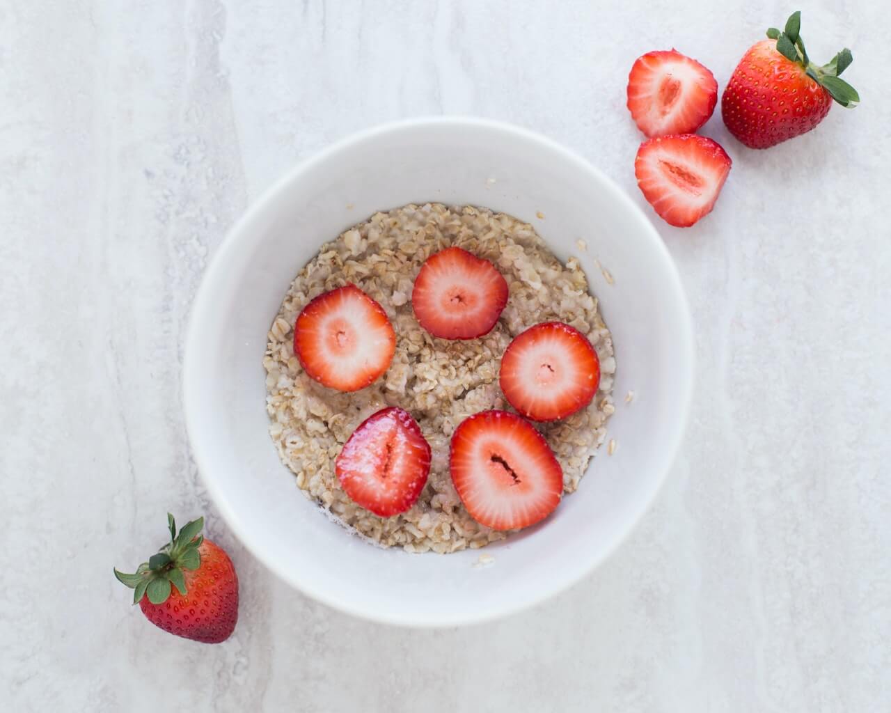 Oatmeal topped with fresh sliced strawberries in a white ceramic bowl