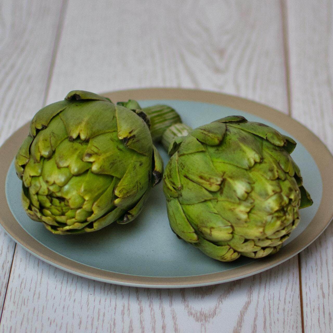 Two fresh green artichokes on a blue ceramic plate