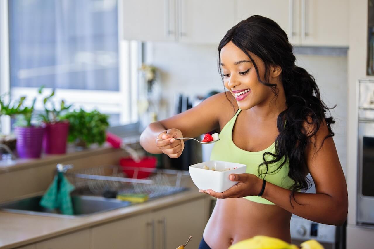 Smiling woman eating breakfast with raspberry in kitchen