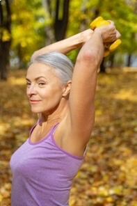 Senior woman stretching and exercising in autumn park with yellow leaves