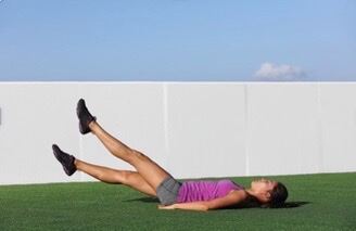 Woman doing core exercise on green mat with raised legs against white wall