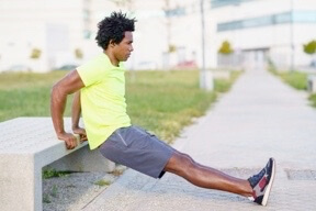 Man in bright yellow shirt does stretching exercise on urban sidewalk