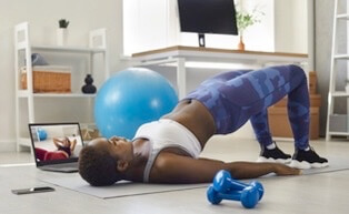 Person doing home workout with exercise ball, laptop, and dumbbells