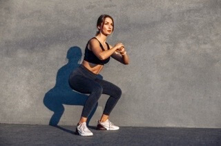 Woman performing squat exercise against gray wall with distinct shadow