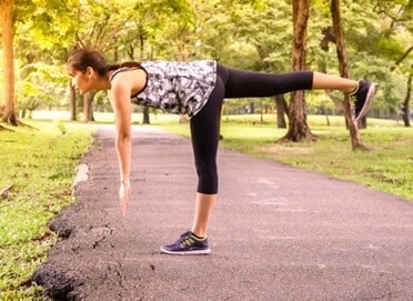 Woman doing yoga balance pose on park path surrounded by trees