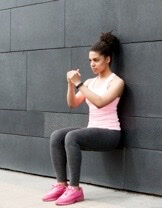 Woman in pink top doing wall sit exercise against gray background