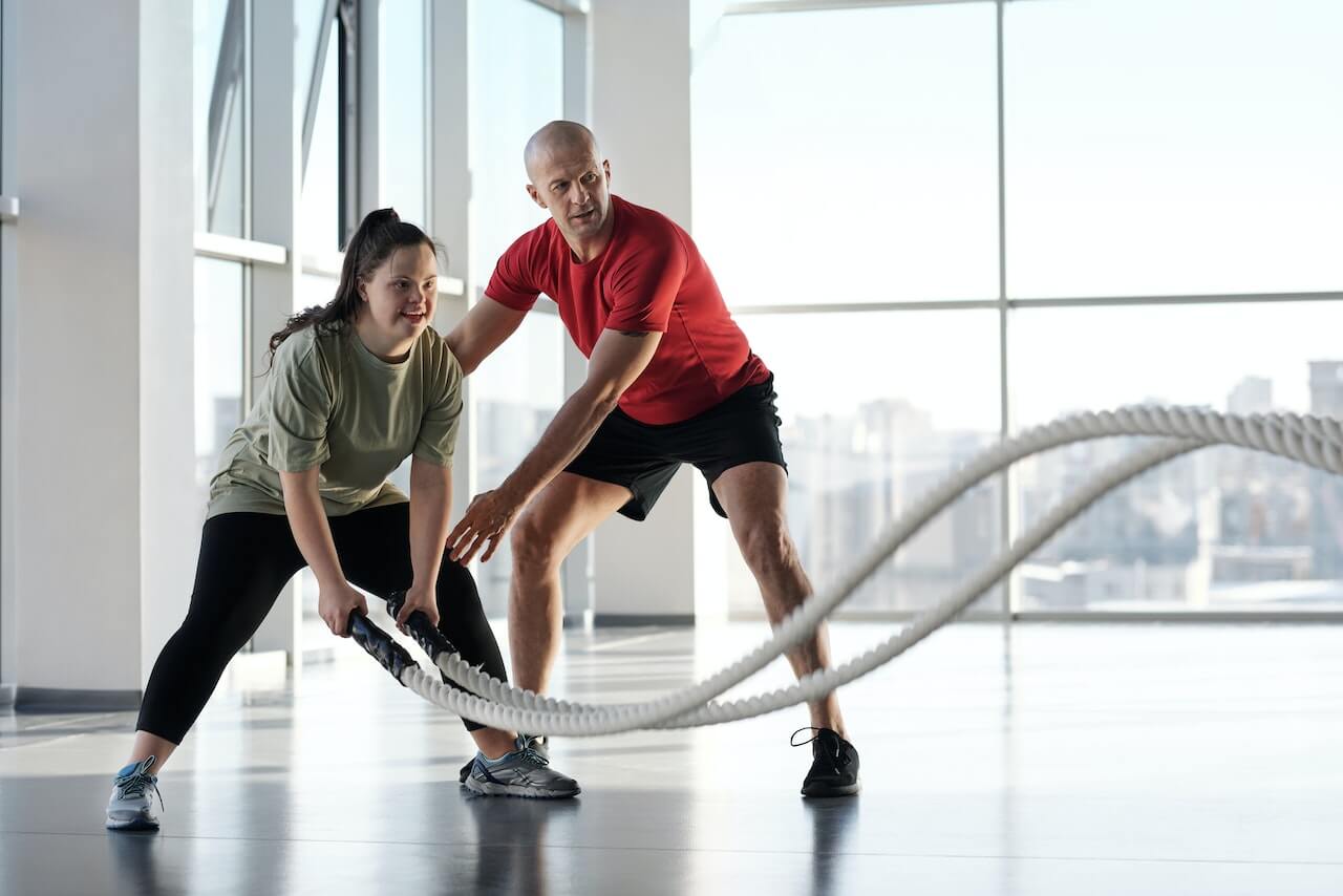 Trainer and client exercising with battle ropes in bright fitness studio