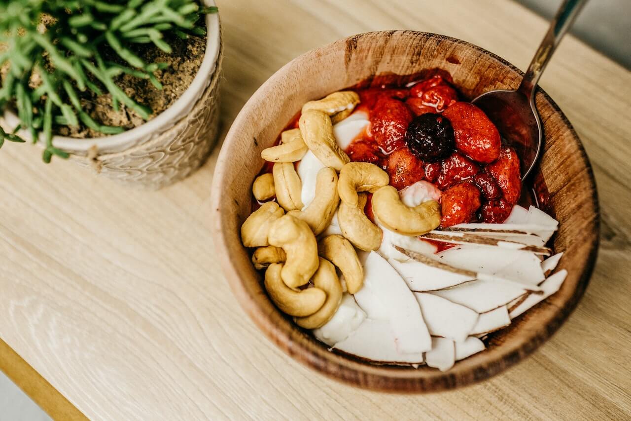 Wooden bowl with cashews, strawberries, coconut flakes, and a spoon