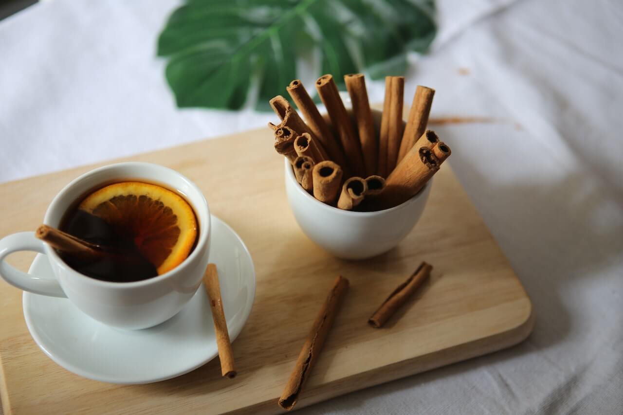 Cup of tea with orange slice and cinnamon sticks on wooden board