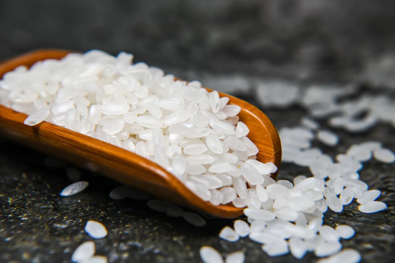 Wooden spoon filled with white rice grains on dark textured surface