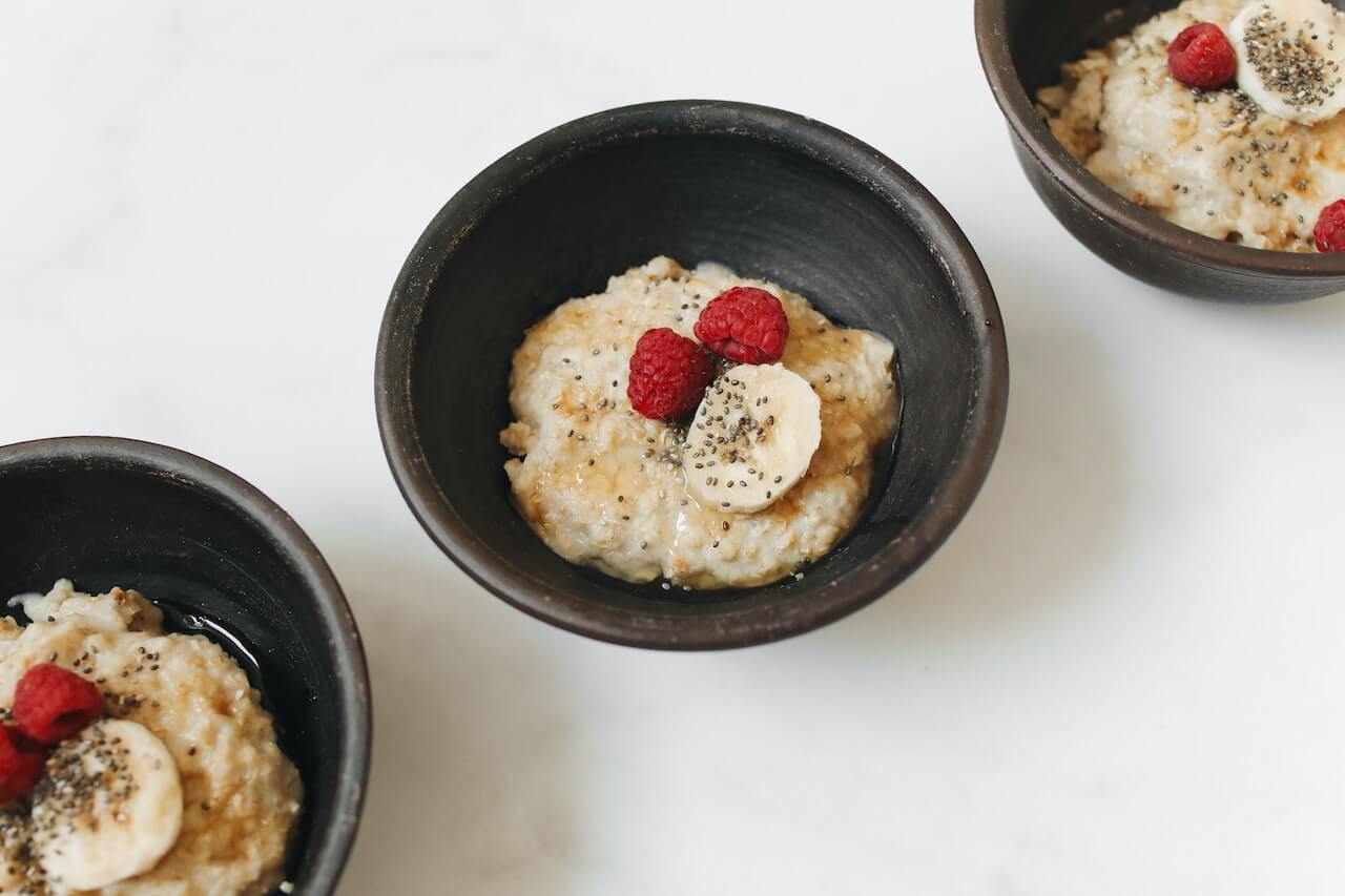 Oatmeal with banana slices, raspberries, and chia seeds in ceramic bowls