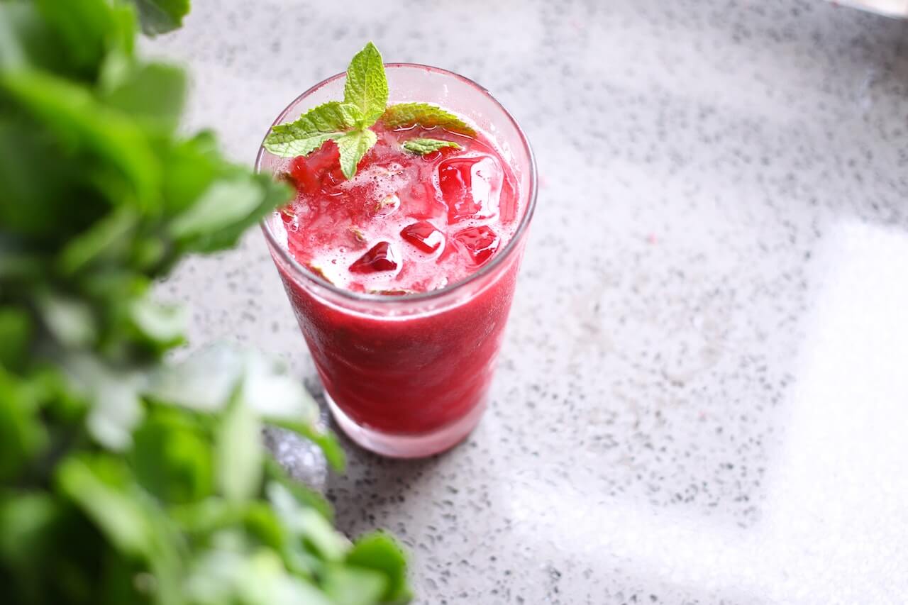 Pink beverage with ice and mint leaves in glass on gray surface
