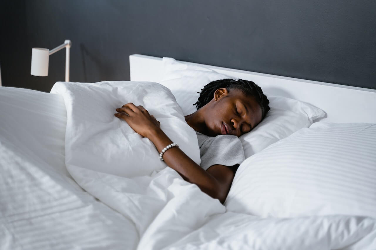 Person sleeping peacefully in white bed with bedside lamp