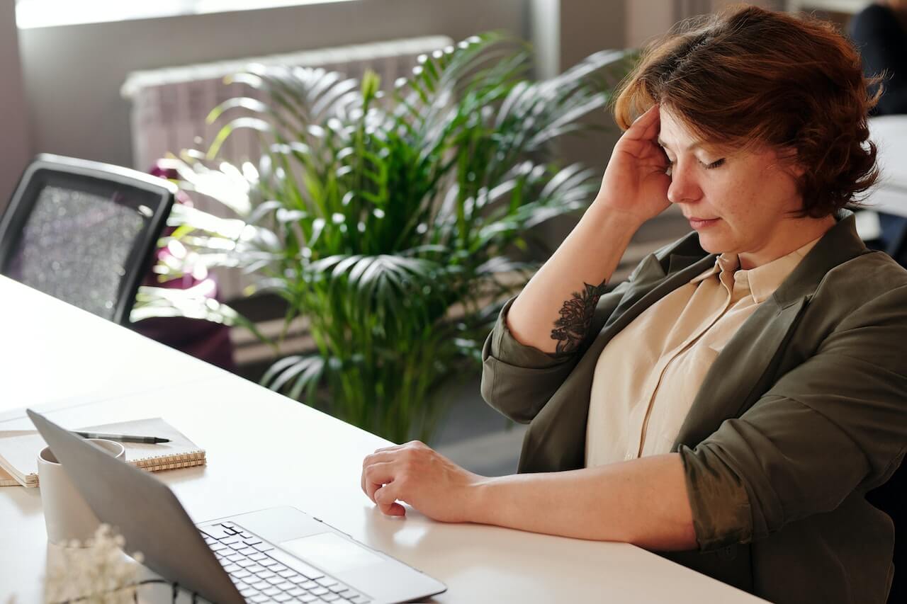 Stressed professional with headache working on laptop in green office