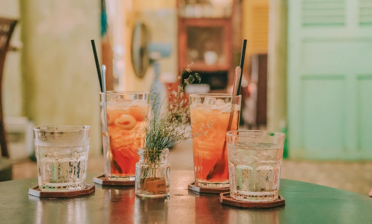 Orange cocktails with ice and straws on wooden coasters, small plant decoration