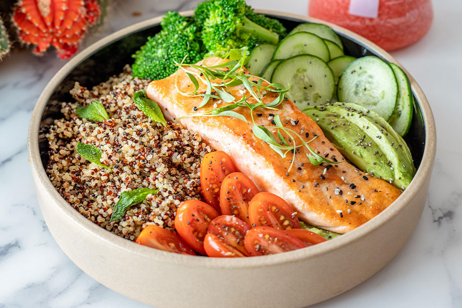 Healthy grain bowl with salmon, quinoa, broccoli, cucumber, and fresh tomatoes
