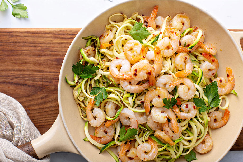 Shrimp and zucchini noodle stir-fry with cilantro garnish in white bowl